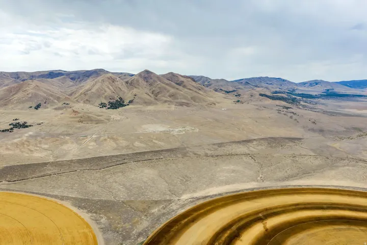 Expansive arid landscape featuring natural mountain formations, scattered green vegetation, and agricultural fields with circular patterns