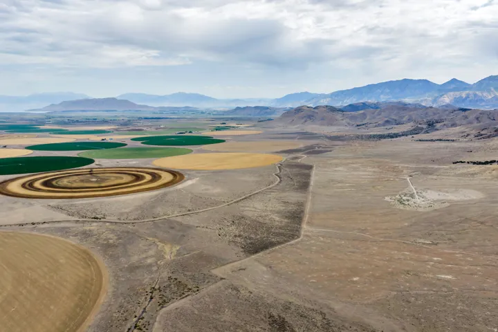 Expansive landscape featuring large circular agricultural fields, surrounding undeveloped land, and distant mountain ranges