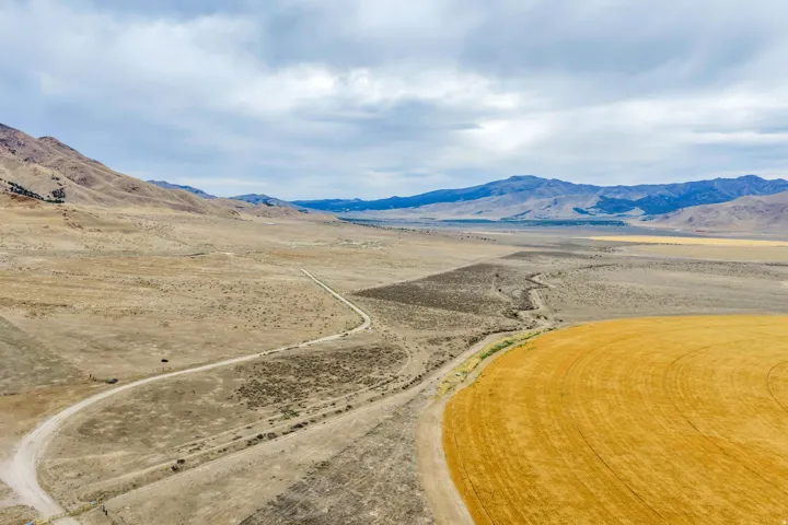 Expansive open land featuring a cultivated circular field, extensive undeveloped terrain, and a winding dirt road