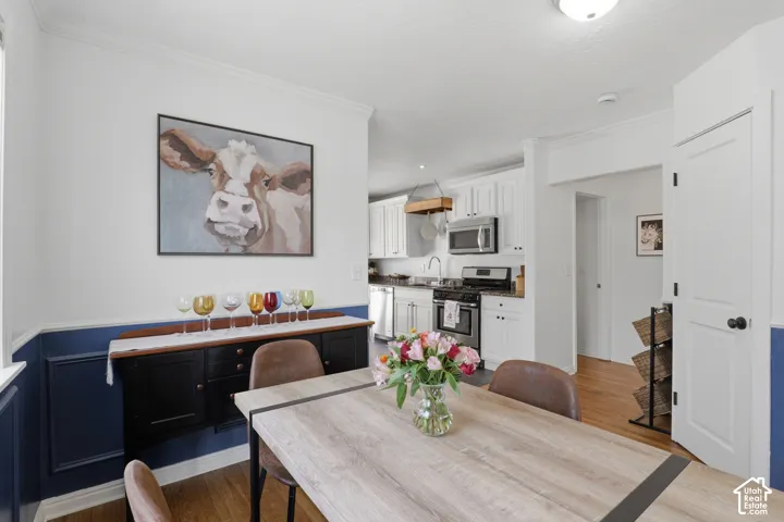 Dining area featuring a wainscoting accent wall in a bold hue, hardwood-finish flooring, and crown molding