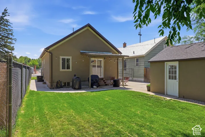 Expansive green lawn with a chain-link fence, a stucco-clad shed featuring a white entry door with glass panes, and a concrete patio extending from the main residence