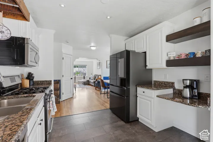 Kitchen featuring granite countertops, white cabinetry, dark wood-finish open shelving, and black appliances