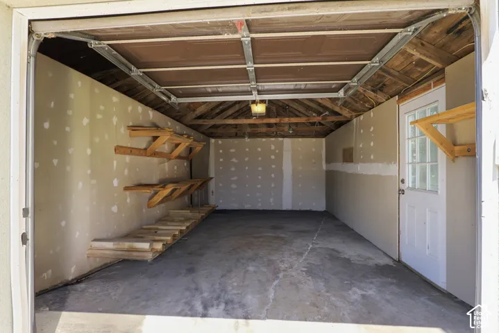 Spacious garage featuring a concrete floor, exposed wood beam ceiling, and built-in shelving