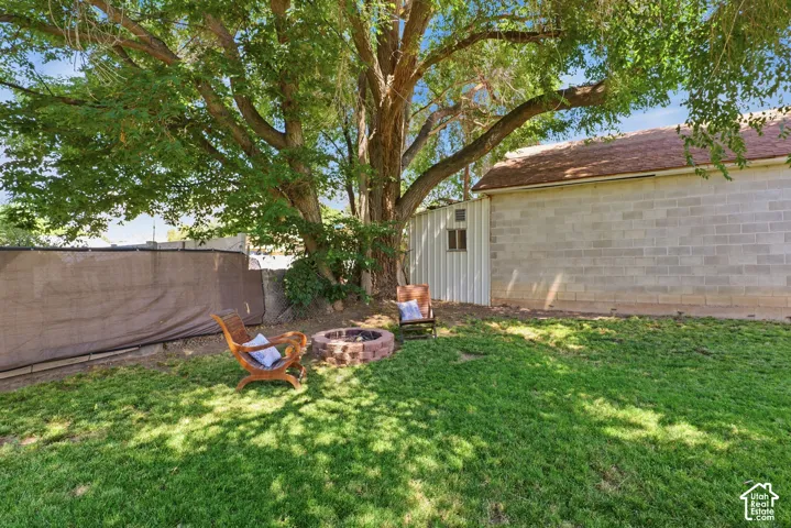 Expansive grassy yard featuring a large mature tree, a stone fire pit, and a chain-link fence with privacy screening