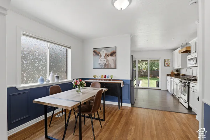 Hardwood flooring extending from the dining area to a kitchen featuring white cabinetry, stainless steel appliances, and a dark countertop