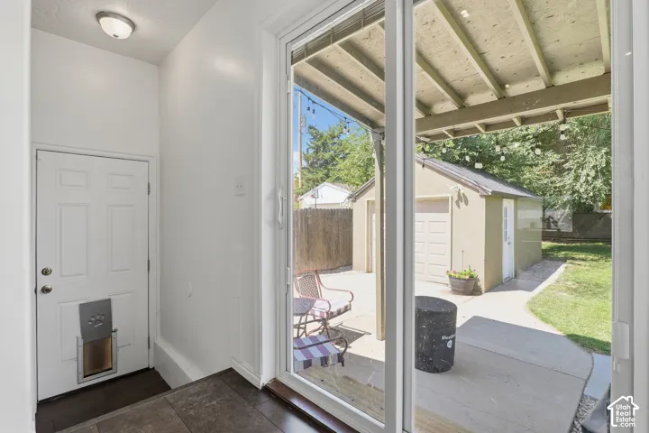 Sliding glass doors opening to a concrete patio, featuring a detached garage with an overhead door and a grassy area beyond