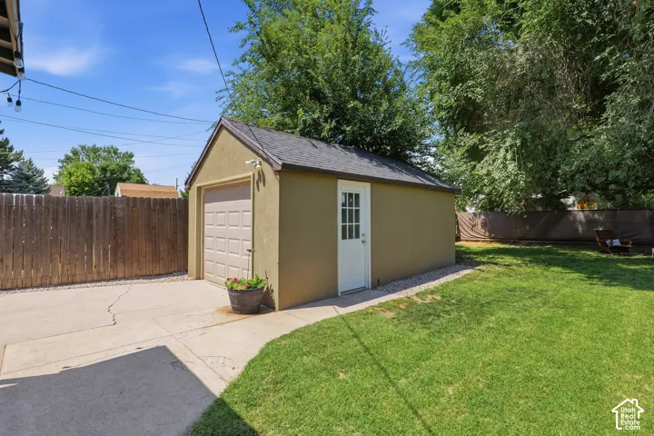 Detached single-car garage featuring a tan exterior, white pedestrian door, and a light-colored garage door