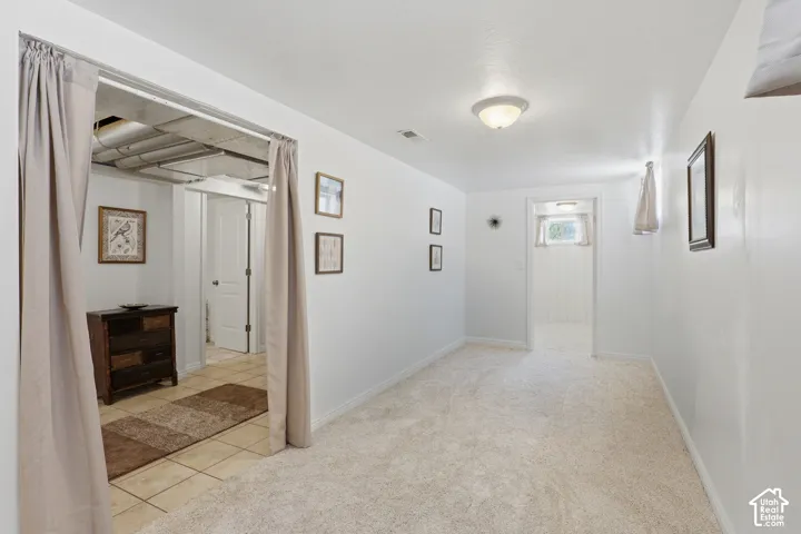 Carpeted room with white walls, a flush-mount ceiling light, and a doorway leading to a tiled area