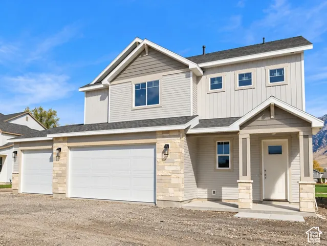 Modern exterior featuring light gray siding, stone accents, two-car garage, covered entry, and a white front door