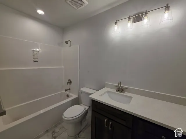 Bathroom featuring a white bathtub and shower surround, a dark wood-finish vanity with a light-colored countertop, and a four-light vanity fixture