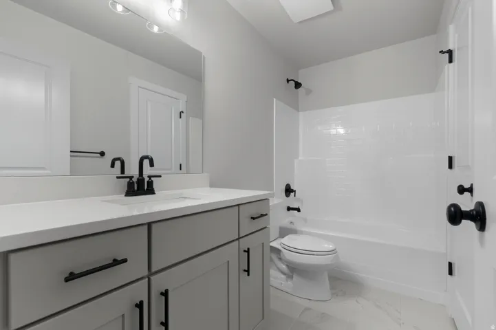 Bathroom featuring a light gray vanity with a white countertop and rectangular sink, matte black fixtures, a white bathtub with subway tile surround, and light tile flooring