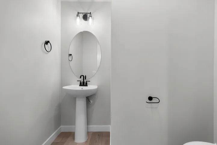 Pedestal sink with matte black faucet, oval mirror, and contemporary two-light fixture