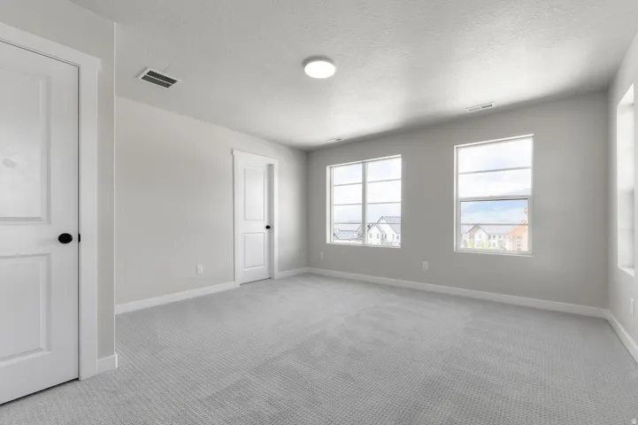 Spacious room featuring light gray carpeting, neutral wall finishes, white trim, and multiple windows