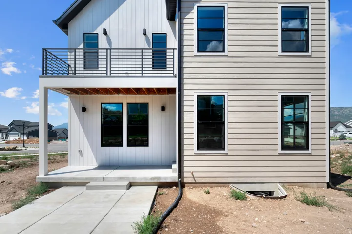Contemporary exterior featuring vertical and horizontal siding, black-framed windows, an upper-level balcony with metal railing, and a ground-level covered patio