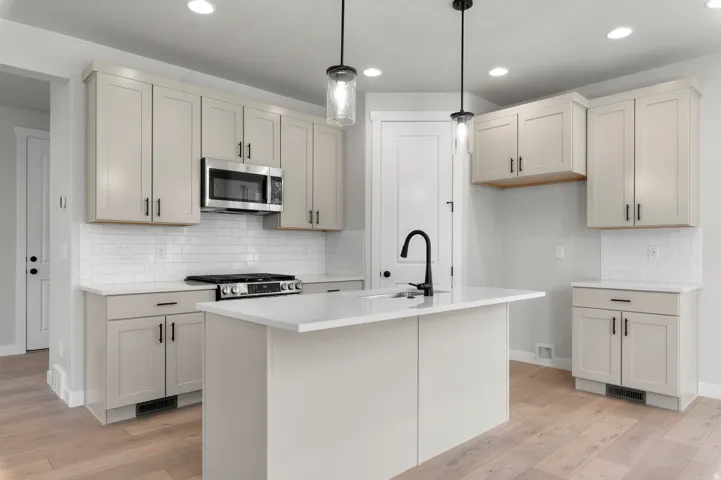 Modern kitchen featuring light cabinetry, white subway tile backsplash, stainless steel microwave, gas range, and a central island with a sink and matte black faucet