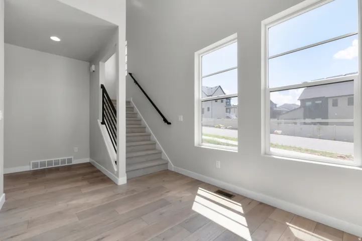 Bright interior space featuring wood-finish flooring, a carpeted staircase with a modern black railing, and recessed lighting