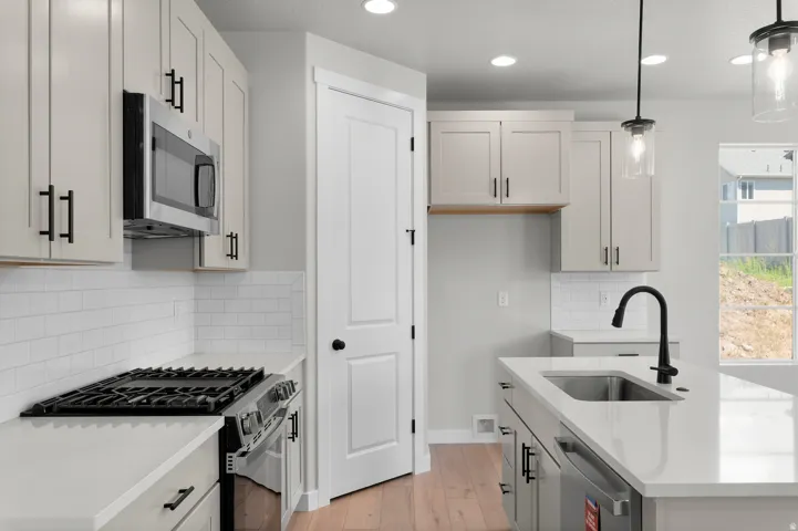 Contemporary kitchen featuring white shaker cabinetry, white subway tile backsplash, stainless steel appliances, a kitchen island with a single basin sink, and wood-finish flooring
