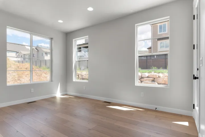 Bright room featuring three large windows, recessed ceiling lighting, wood-finish flooring, and light-colored walls