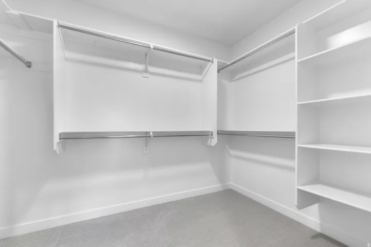 Walk-in closet featuring built-in shelving, multiple hanging rods, white walls, white baseboards, and light gray carpeting