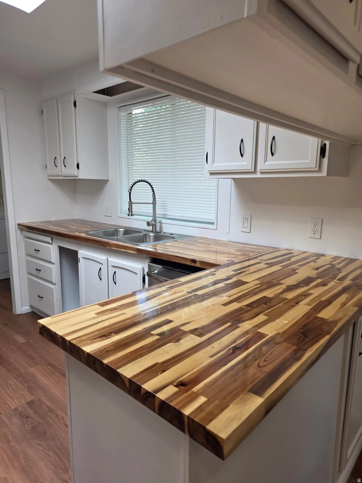 Kitchen featuring wood-finish countertops, white cabinetry with dark hardware, a double basin sink with a high arc faucet, and a window with horizontal blinds