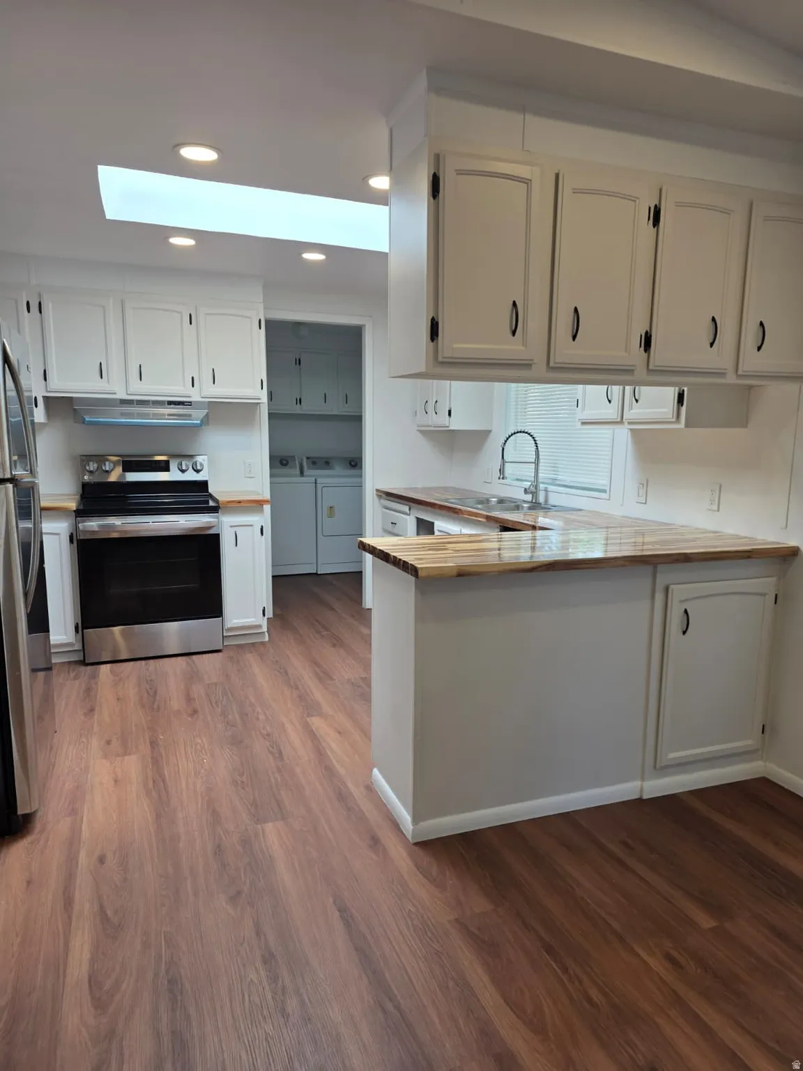 Kitchen featuring wood-finish flooring, white cabinetry, stainless steel appliances, and a skylight