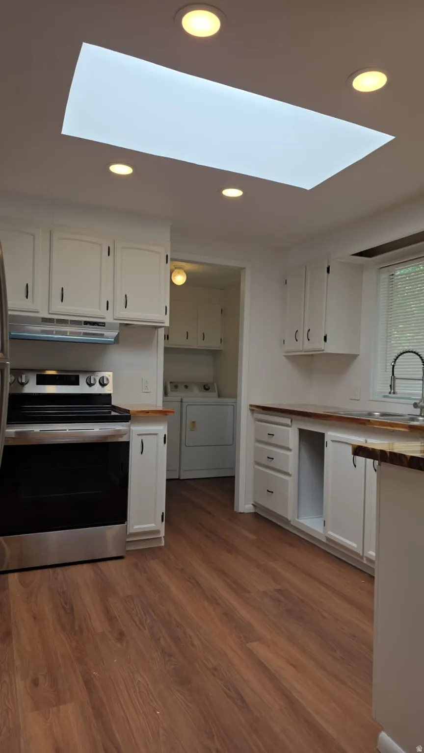 Kitchen featuring wood-finish flooring, white cabinetry, a stainless steel range, and a rectangular skylight