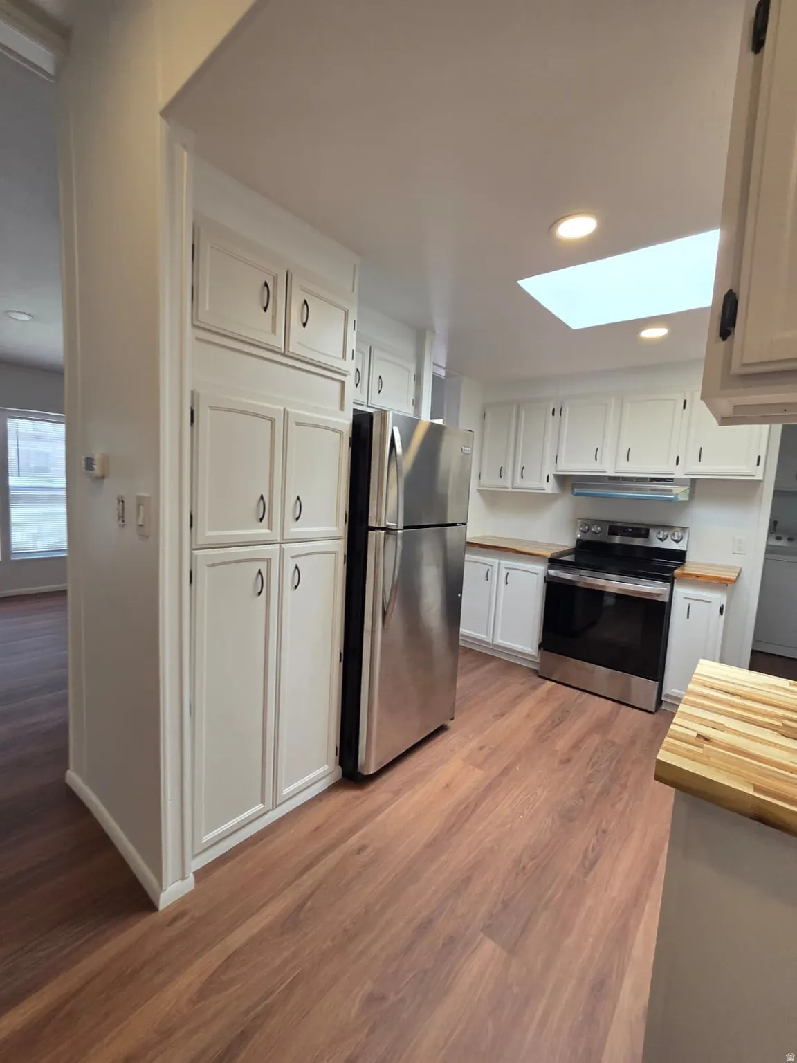 Kitchen featuring wood-finish flooring, white cabinetry, stainless steel appliances, and a ceiling skylight