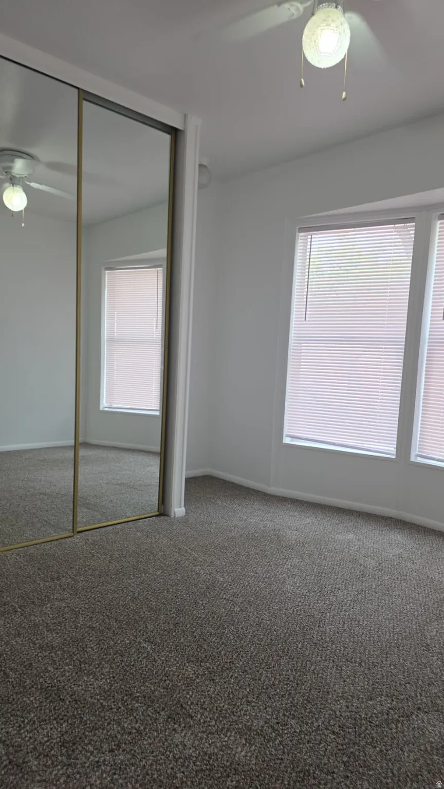 Carpeted room featuring a ceiling fan with integrated lighting, two windows with blinds, and mirrored sliding closet doors