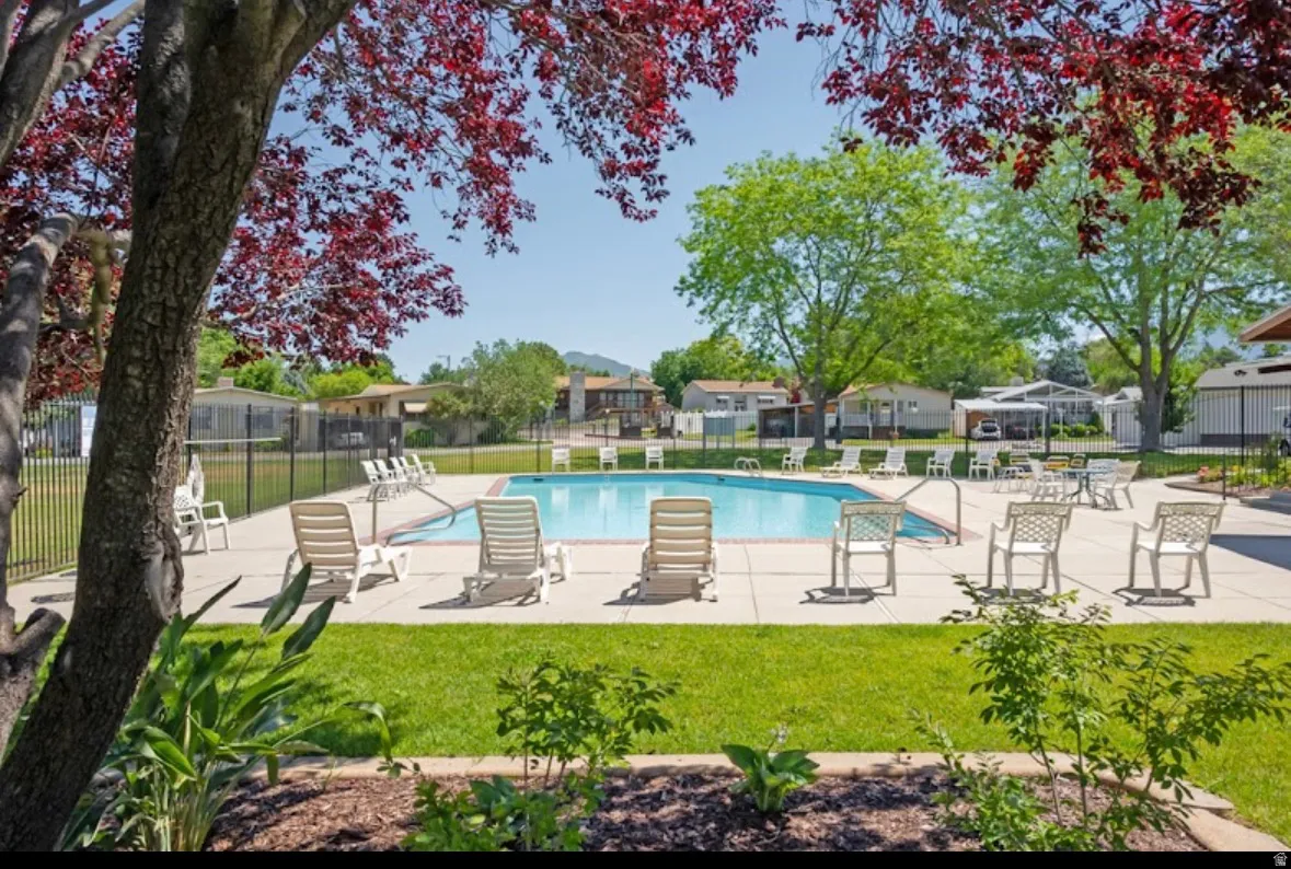Outdoor swimming pool with surrounding concrete patio, bordered by a black metal fence