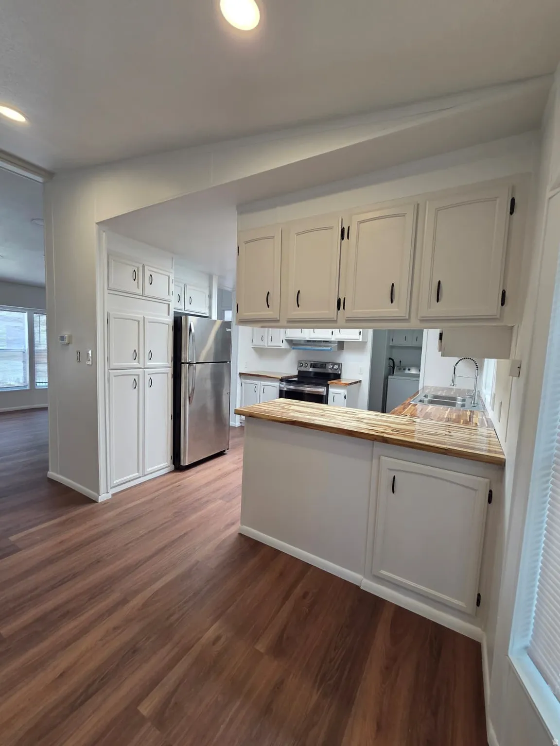 Kitchen featuring wood-finish flooring, white cabinetry, stainless steel appliances, and a wood countertop