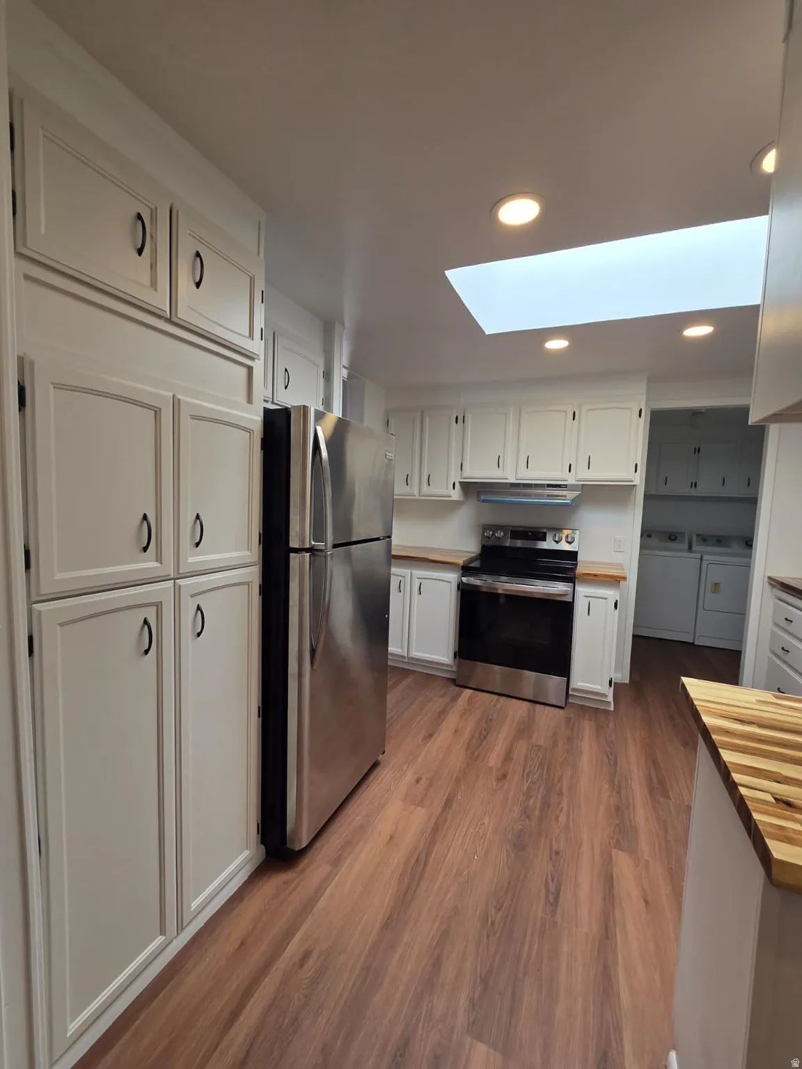 Kitchen featuring flooring, white cabinetry with black hardware, stainless steel appliances, a skylight, and recessed lighting