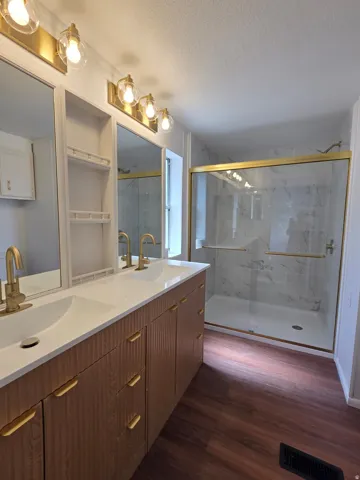 Dual vanity with wood-finish cabinetry, integrated sinks, and gold-tone fixtures