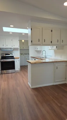 Kitchen featuring wood-finish flooring, white cabinetry with dark hardware, a stainless steel range, and butcher block-style countertops