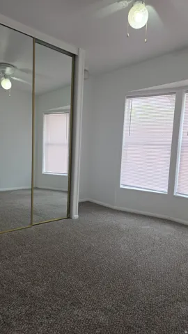 Carpeted room featuring a ceiling fan with integrated lighting, two windows with blinds, and mirrored sliding closet doors