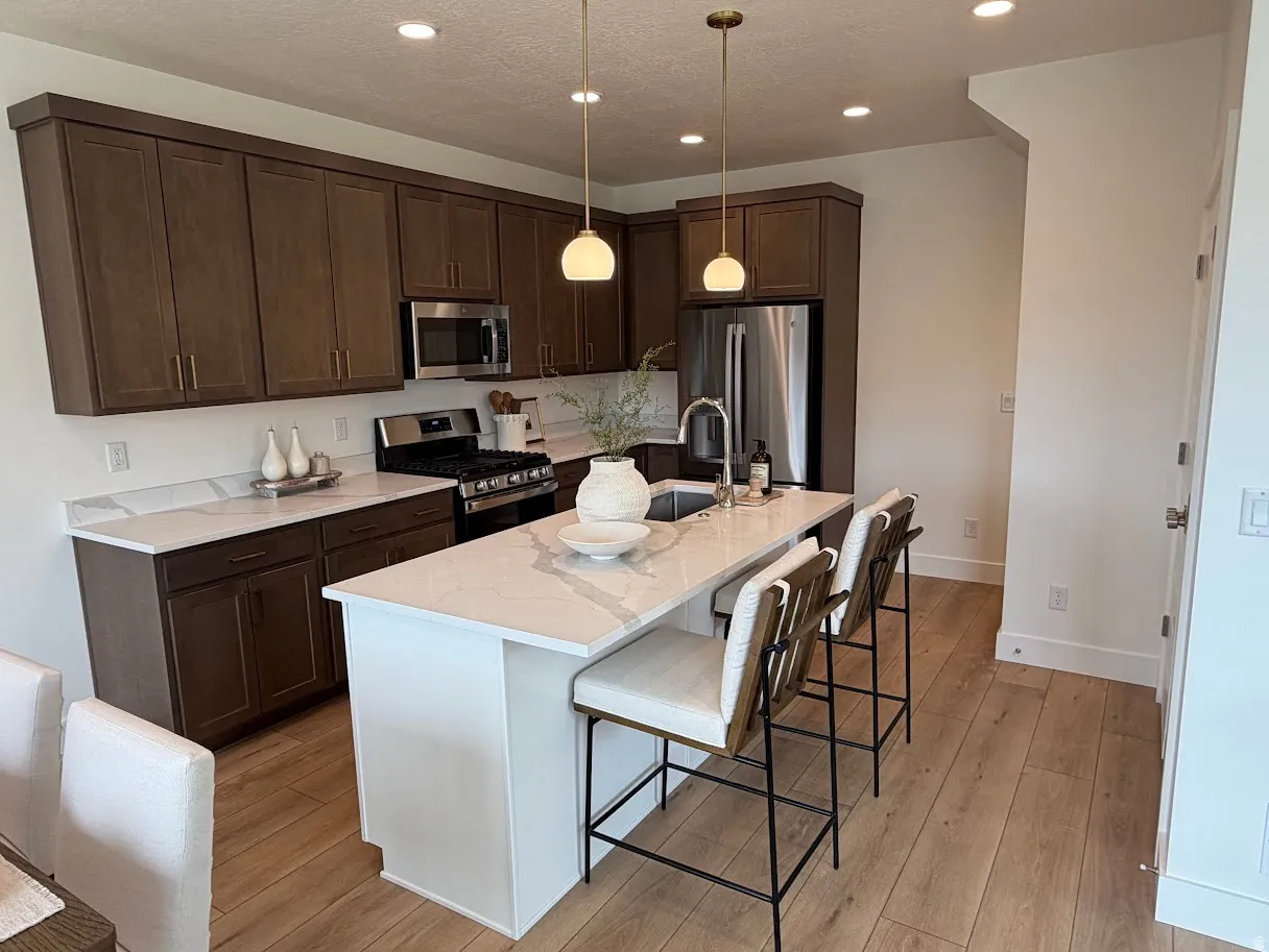 Kitchen featuring an island with seating, stainless steel appliances, dark wood-finish cabinetry, light stone countertops, and wood-finish flooring
