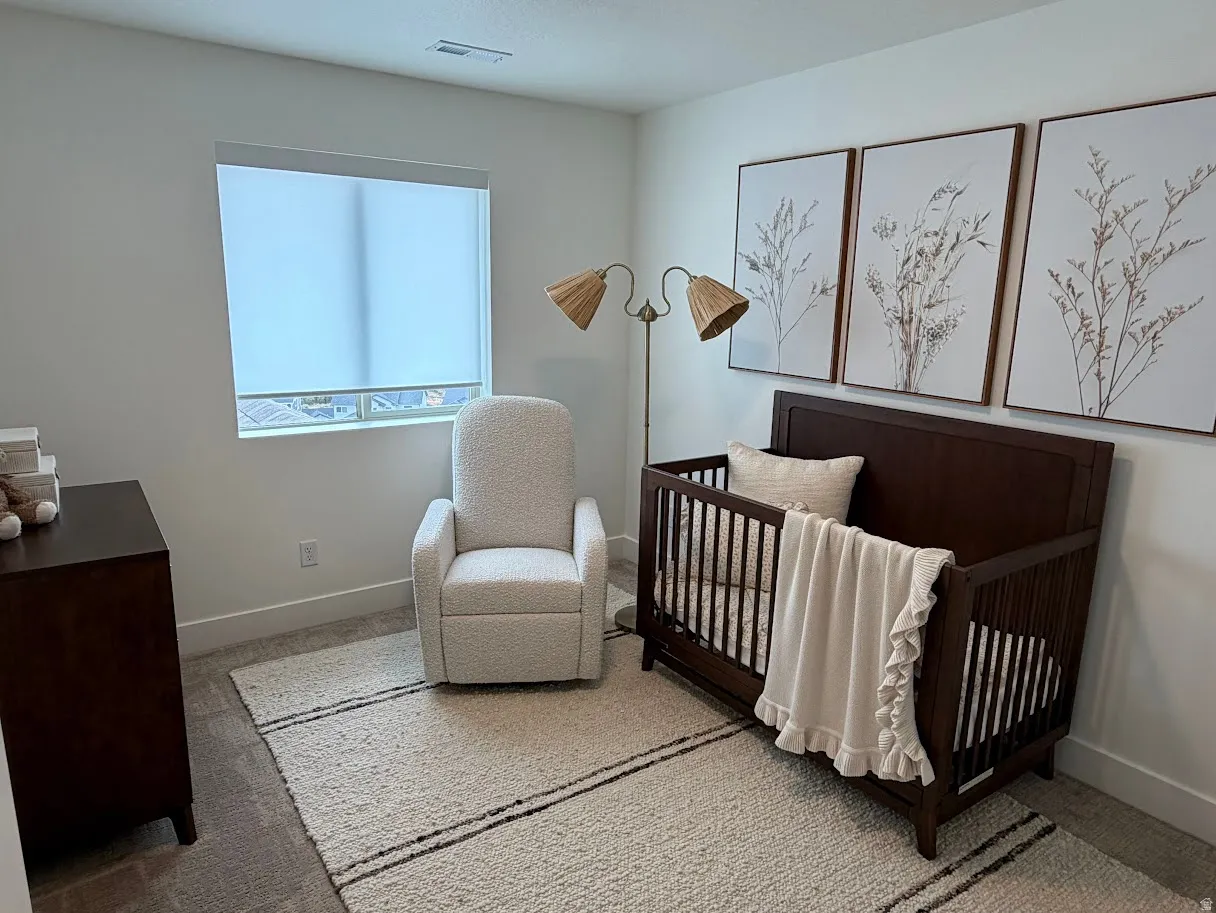 Carpeted room with a large window featuring a roller shade, white baseboards, and light wall paint