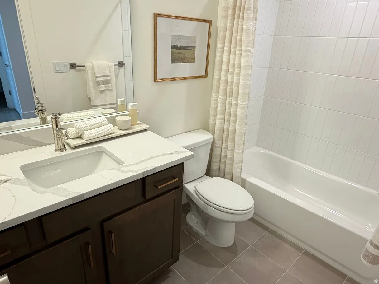 Bathroom featuring a vanity with a white countertop and integrated sink, dark wood-finish cabinetry, a built-in tub with white subway tile surround, and neutral floor tiling