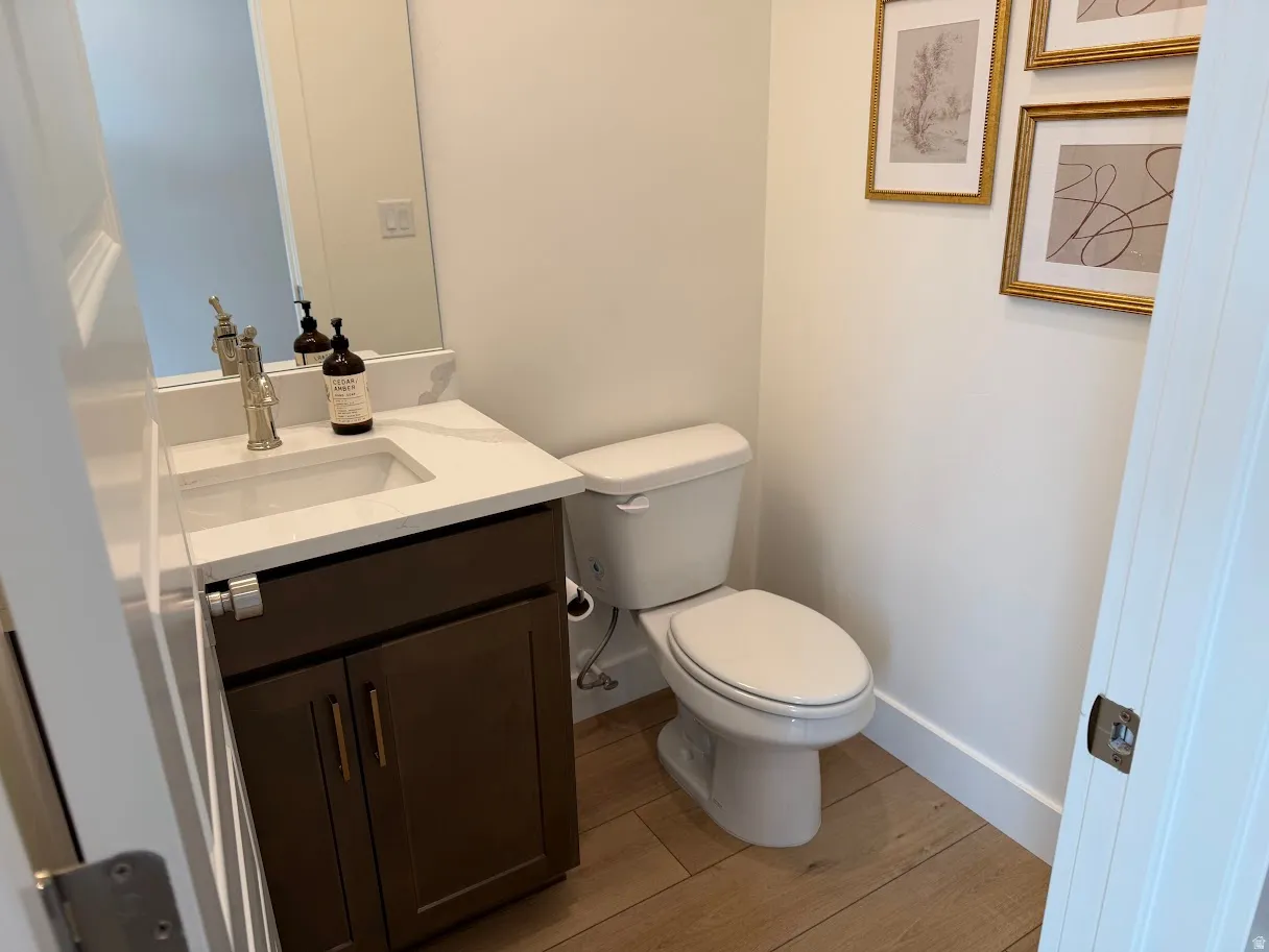 Powder room featuring a single vanity with a white countertop, built-in sink, and bronze-finish hardware, complemented by wood-finish flooring and a toilet