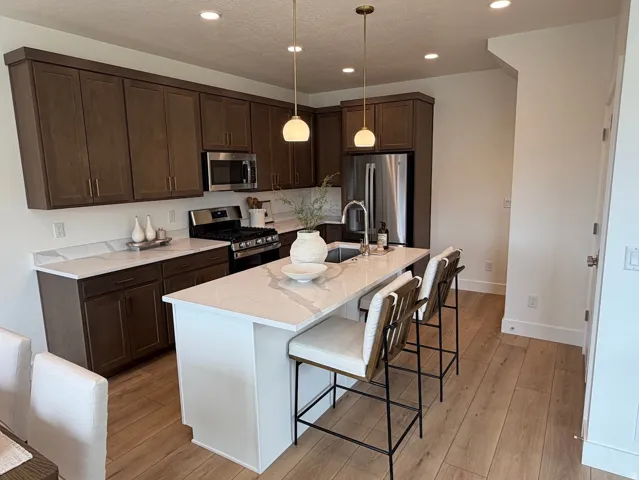 Kitchen featuring an island with seating, stainless steel appliances, dark wood-finish cabinetry, light stone countertops, and wood-finish flooring