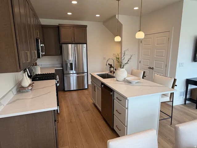 Contemporary kitchen featuring wood-finish flooring, white countertops with veining, and a central island with integrated sink