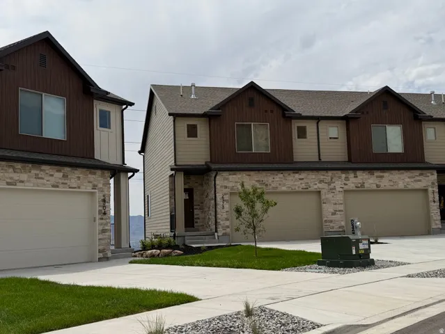 Modern townhome exterior featuring a stone and siding facade, attached two-car garage, and landscaped front yard with concrete driveway
