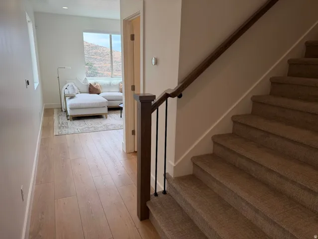 Wood-finish flooring extending from the entry, with a carpeted staircase featuring a dark wood handrail and black metal balusters