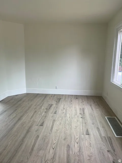 Neutral-toned room featuring light wood-finish flooring, white baseboards, and a window with white trim
