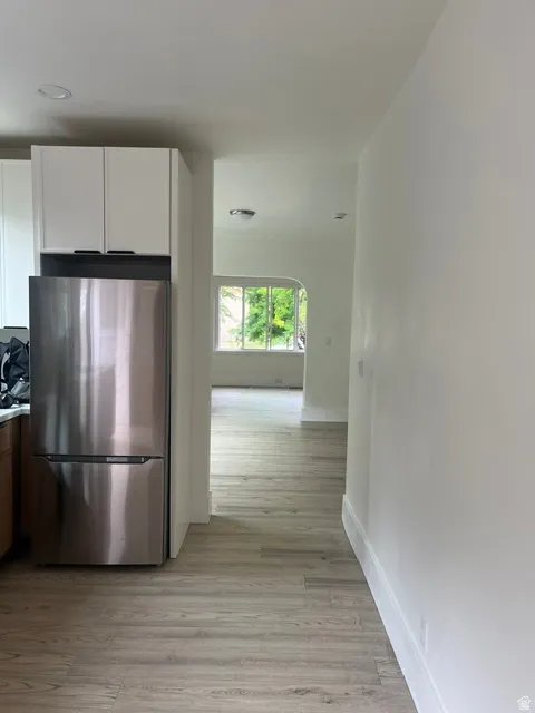 Kitchen featuring a stainless steel refrigerator, white upper cabinetry, and wood-finish flooring