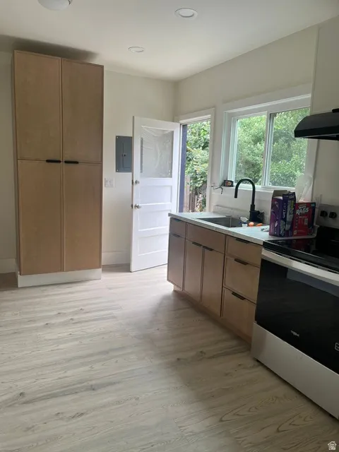 Kitchen area featuring light wood-finish cabinetry, a black range hood, a stainless steel sink with a black faucet, light countertops, and light wood-finish flooring