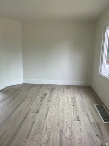 Neutral-toned room featuring light wood-finish flooring, white baseboards, and a window with white trim