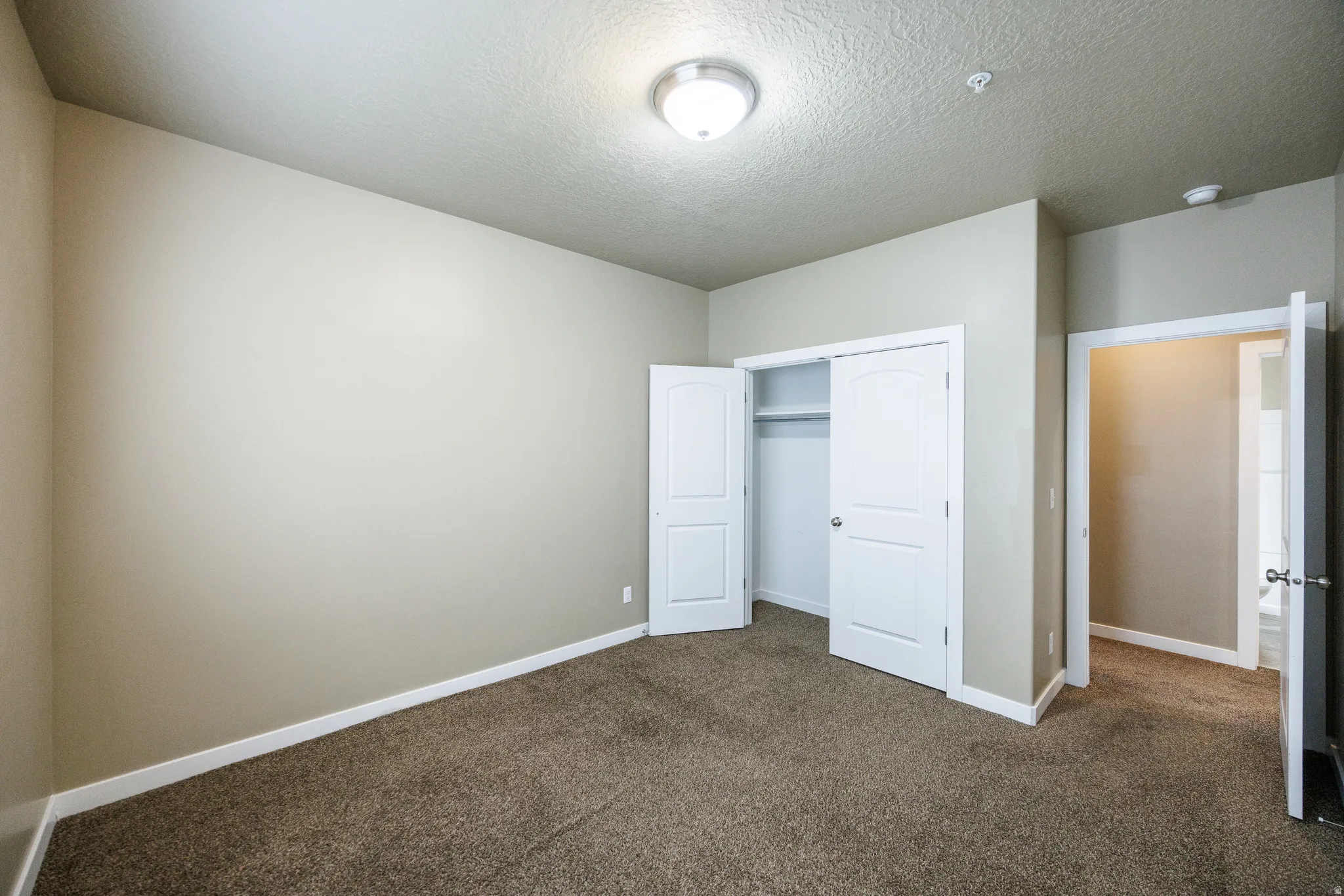 Neutral-toned room featuring a vaulted ceiling and textured carpet flooring