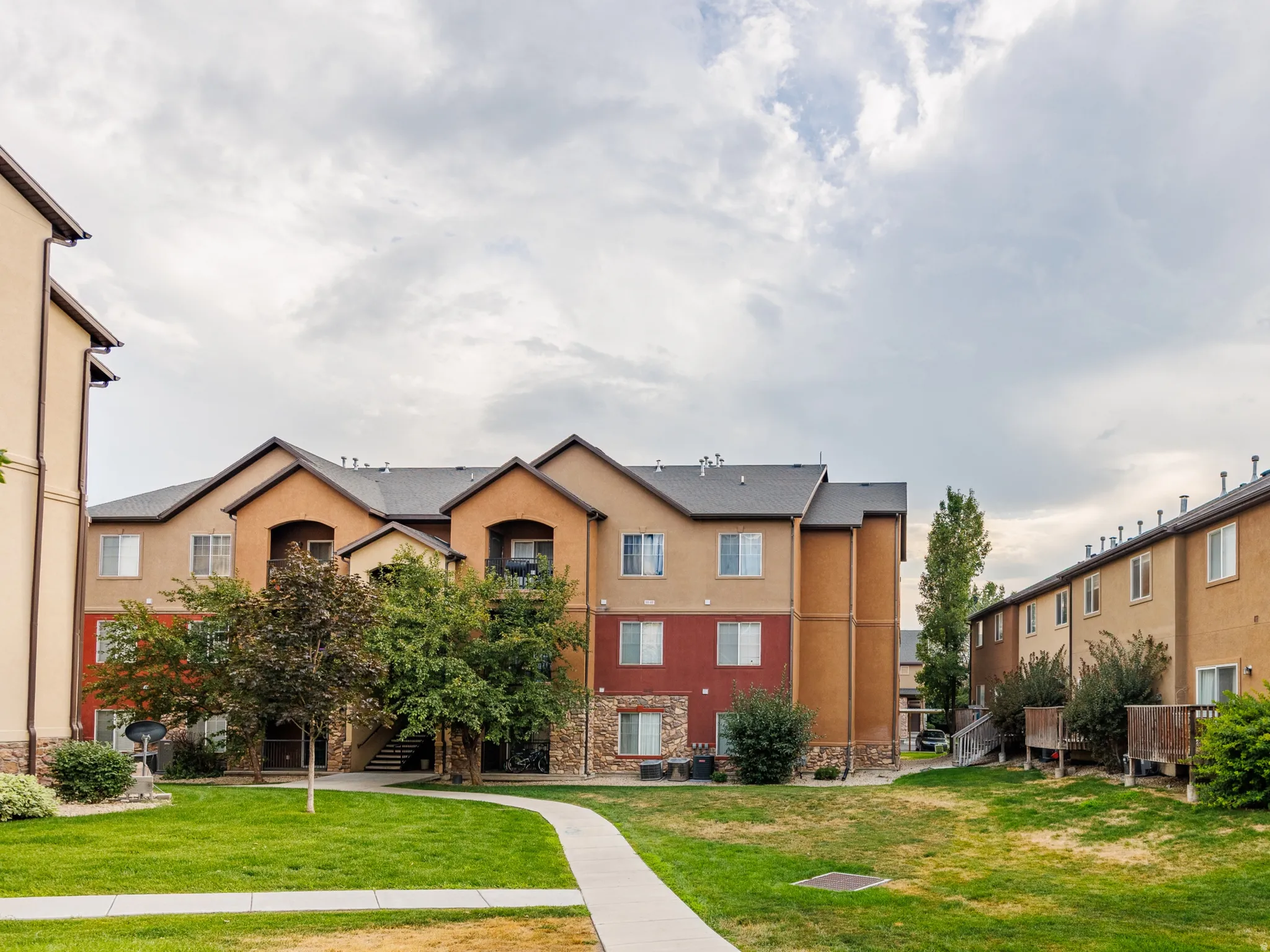 Manicured green space with concrete pathways surrounded by multi-story residential buildings featuring stucco and stone veneer exteriors