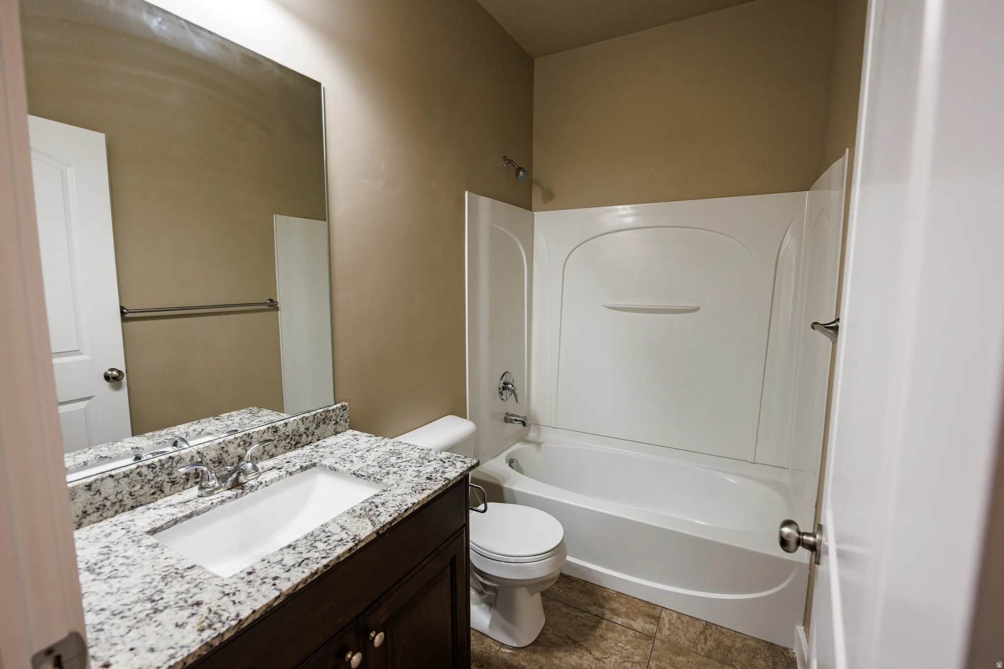 Bathroom featuring a white bathtub and shower surround, a toilet, and a vanity with a white rectangular sink, granite-finish countertop, and dark wood-finish cabinetry