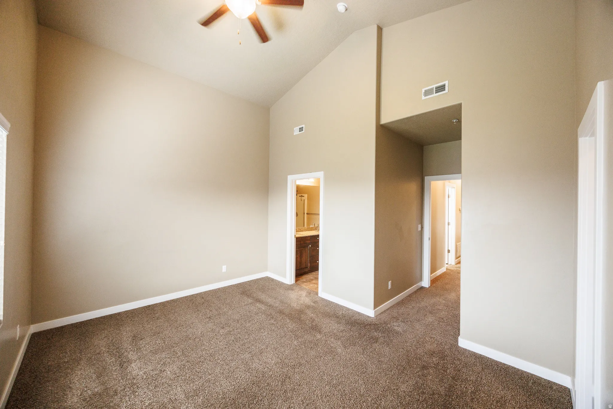 Carpeted interior space featuring vaulted ceilings, a ceiling fan with integrated lighting, and multiple doorways